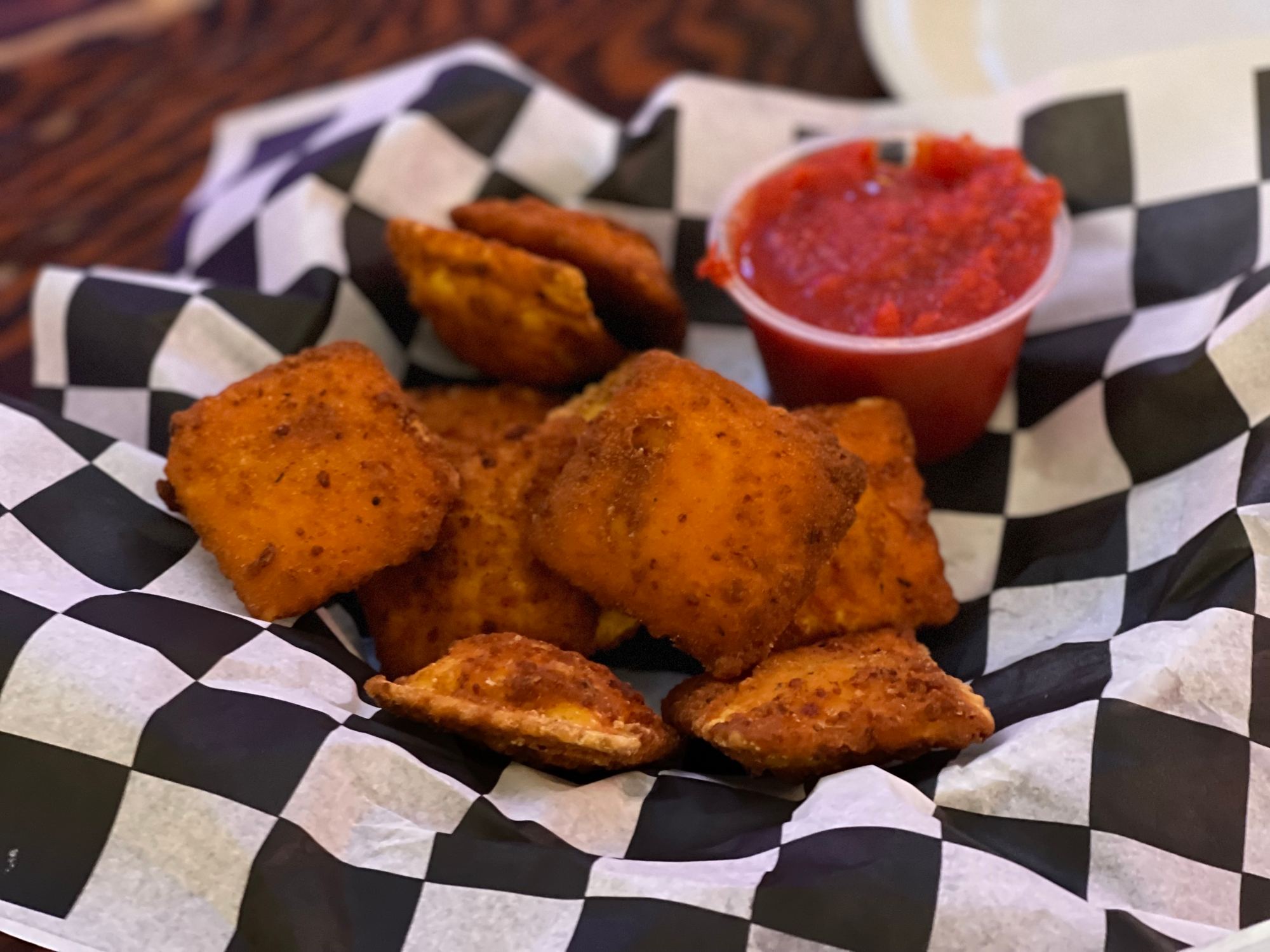 A basket of toasted ravioli with a cup of marinara sauce for dipping