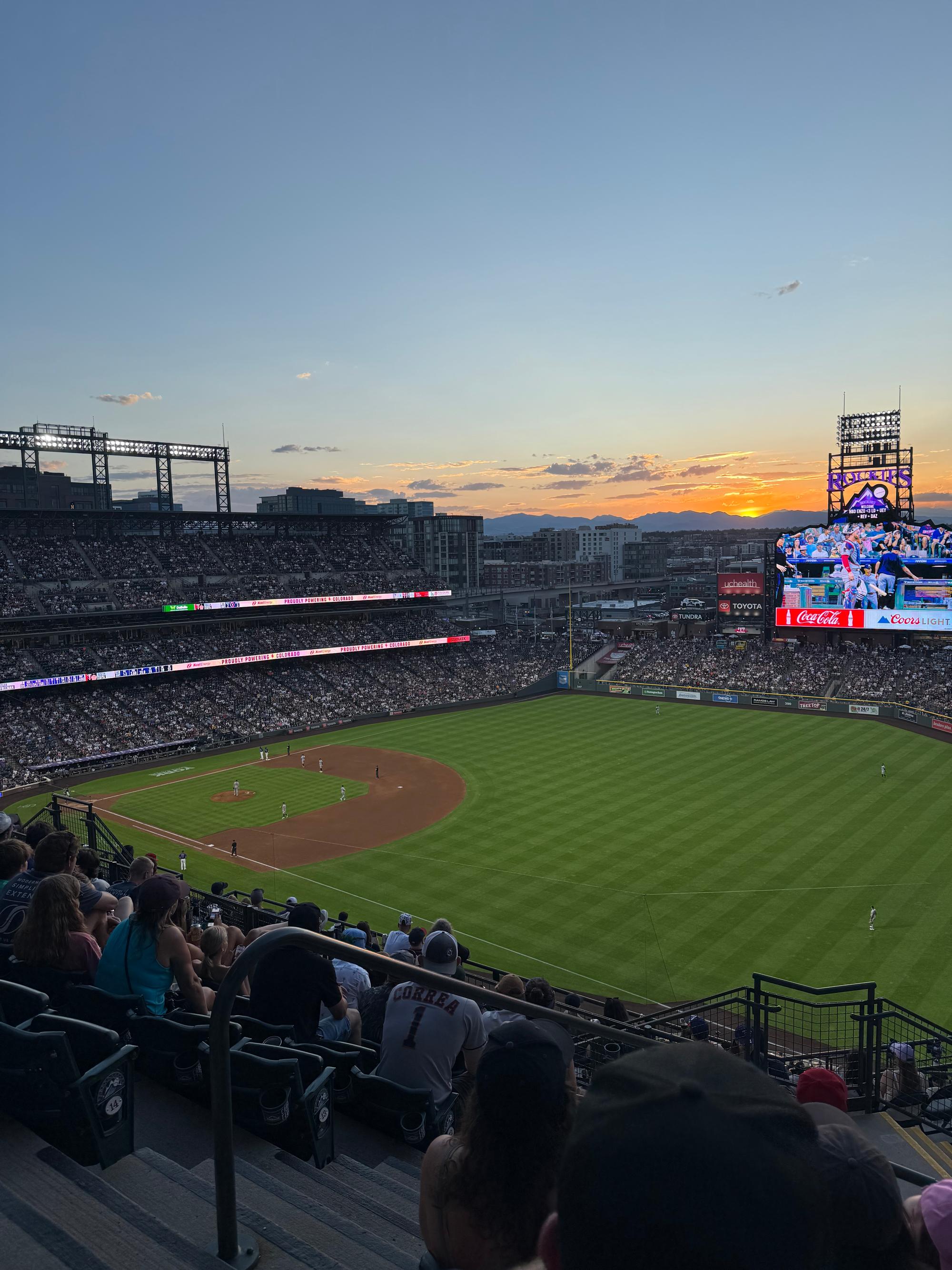 A game at Coors Field at sunset, with the mountains on the horizon behind the lit videoboard