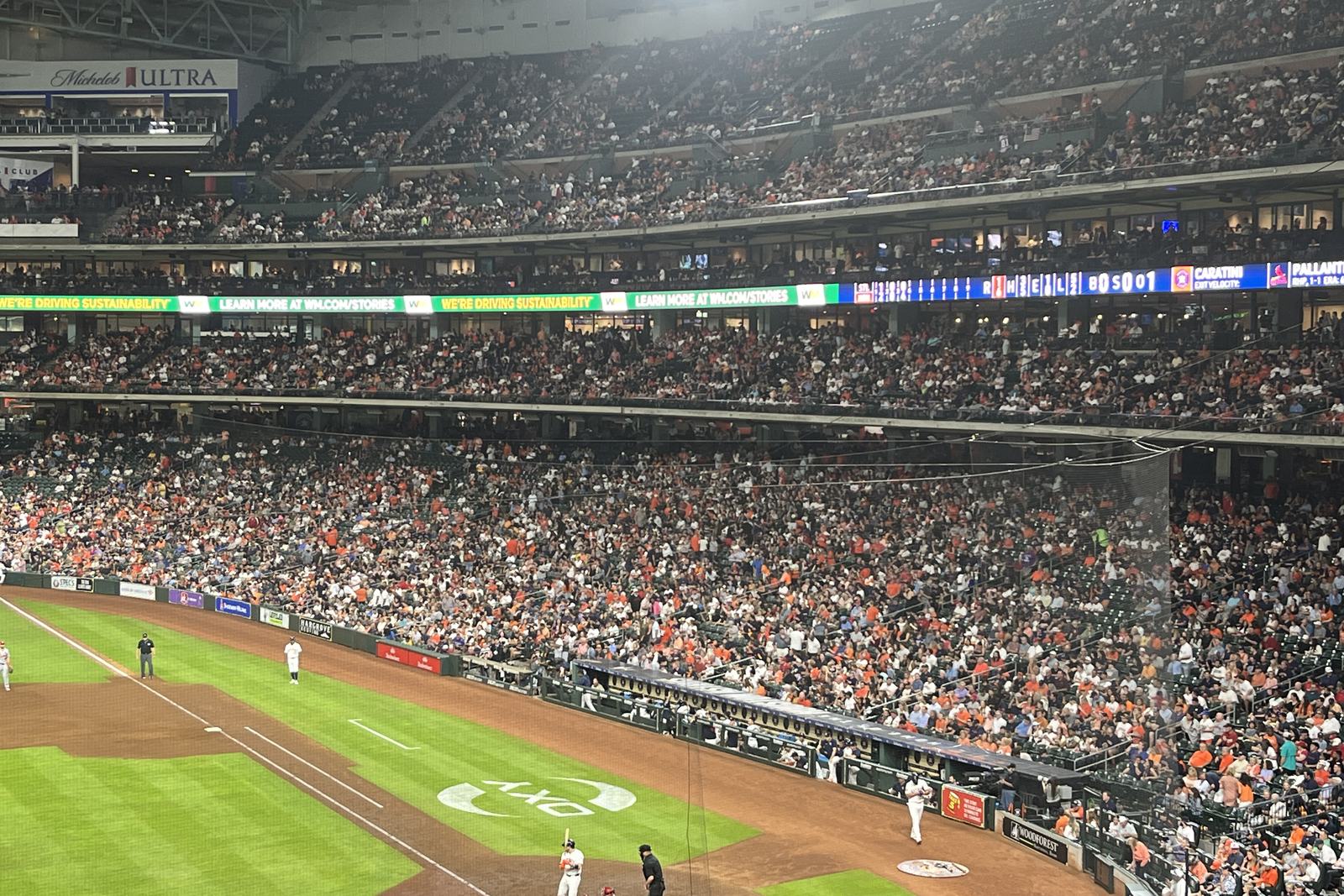 A packed three-deck grandstand at Daikin Park during a night game, fans filling the lower bowl, the club level and the upper deck along the first-base line