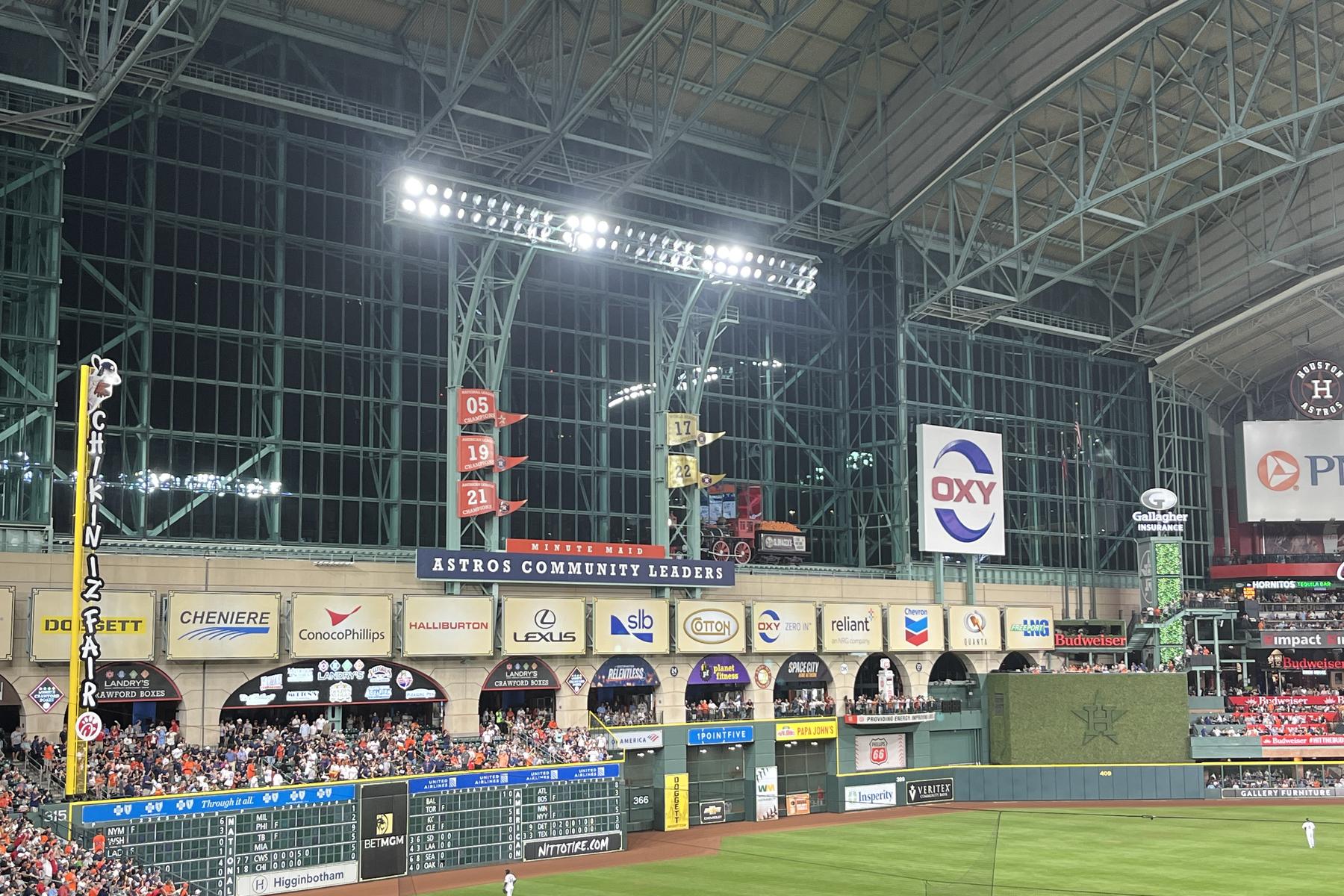The closed roof over Daikin Park lit for a night game, the replica train on its track above the left-field wall, the Crawford Boxes below it, and the 2005, 2019 and 2021 pennants hanging from the roof truss