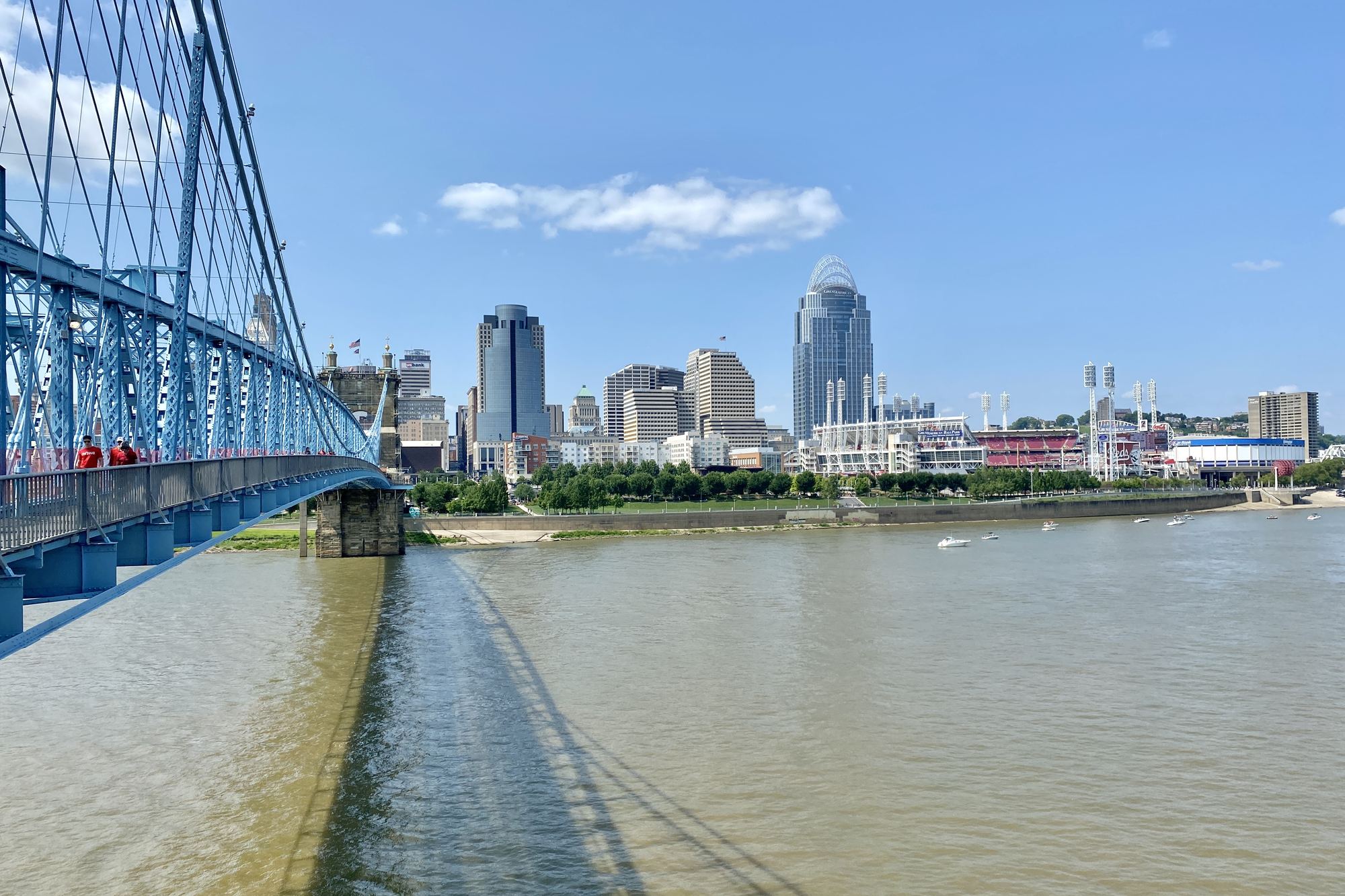 Great American Ball Park and the downtown Cincinnati skyline seen from the Roebling Suspension Bridge across the Ohio River, the bridge's blue steel and cables running through the foreground