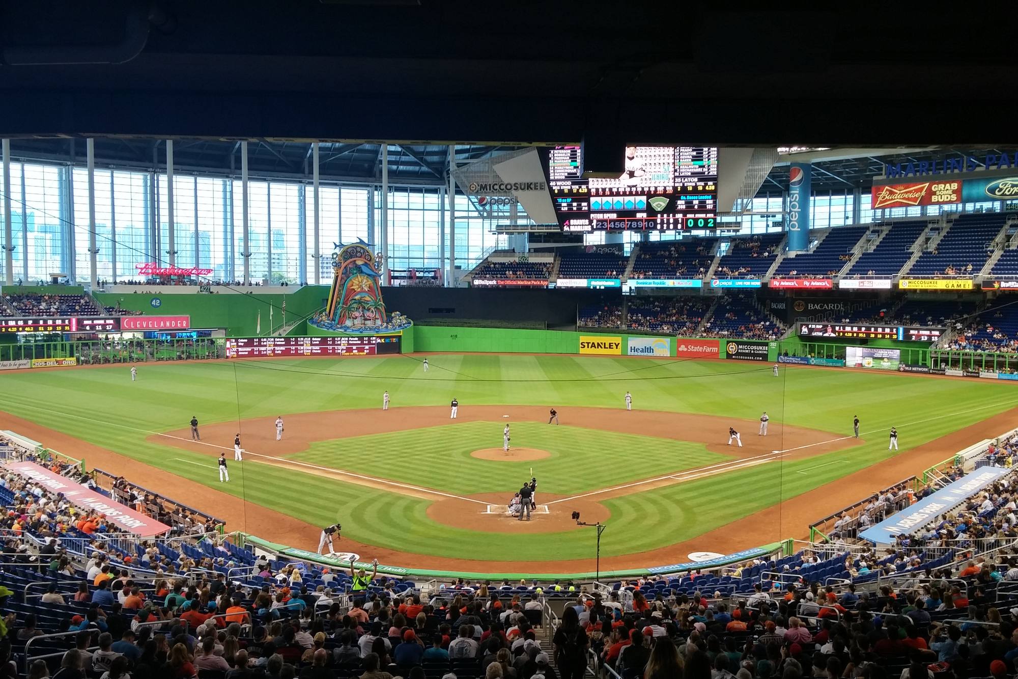 A full bowl at loanDepot park with the six glass panels of the Left Field Operable Wall open onto the downtown Miami skyline, the roof closed overhead and the Home Run Sculpture standing behind the center-field wall