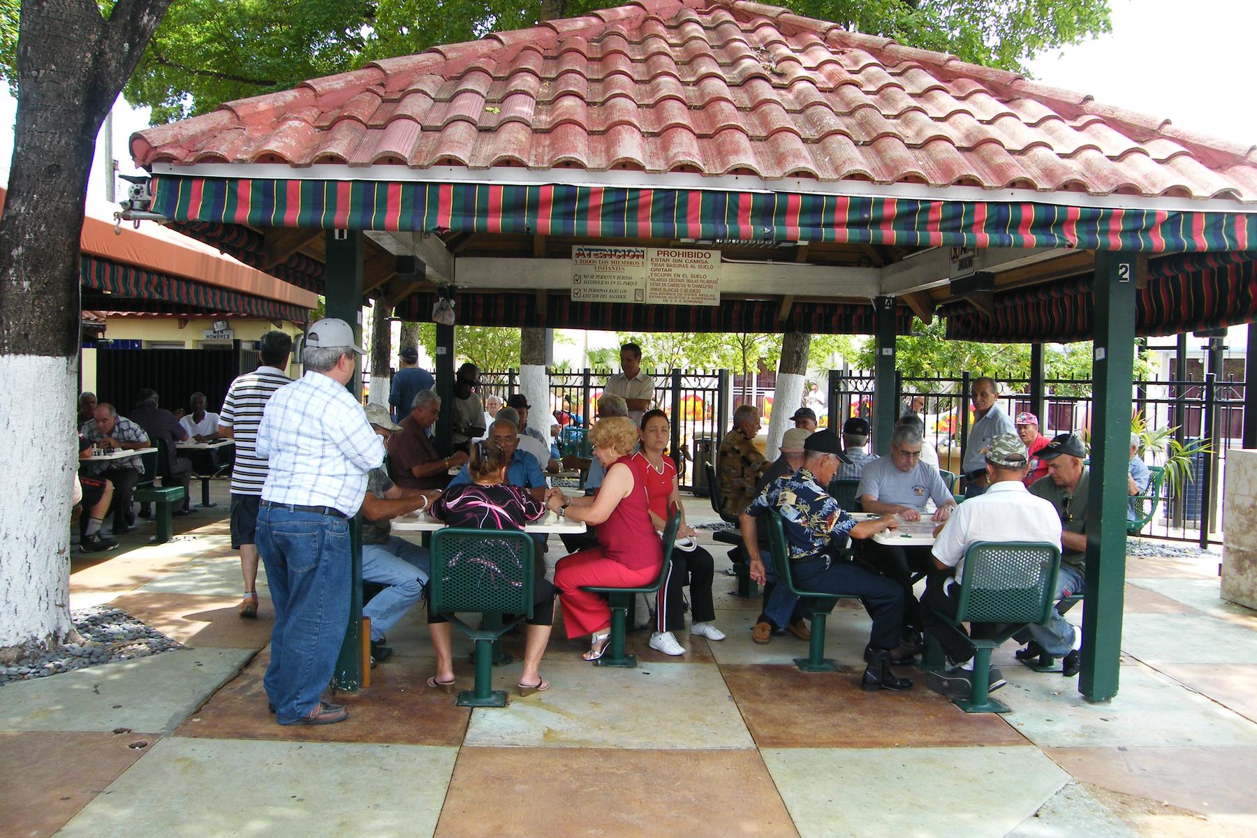 Every table full under the tiled pavilion at Domino Park on Calle Ocho, players and onlookers crowded around the boards, the house rules posted in Spanish on the center post