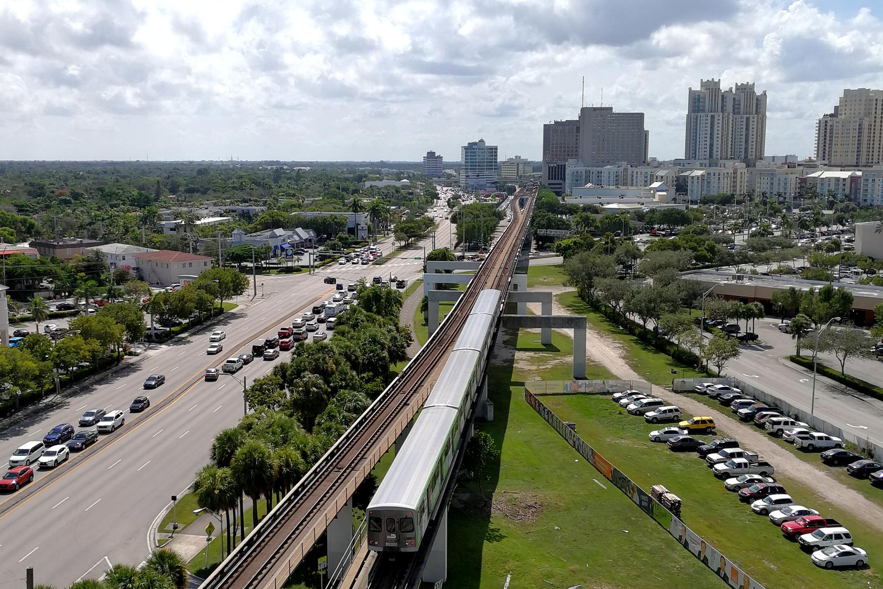 A Metrorail train running on its elevated concrete guideway above a Miami street, six lanes of stopped traffic backed up alongside it