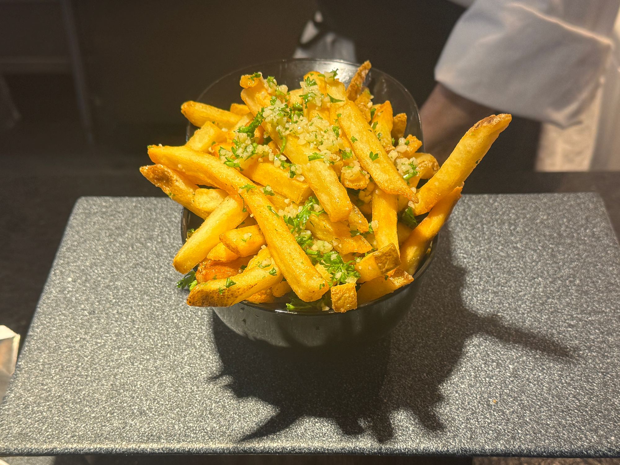A cup of garlic fries topped with chopped garlic and parsley