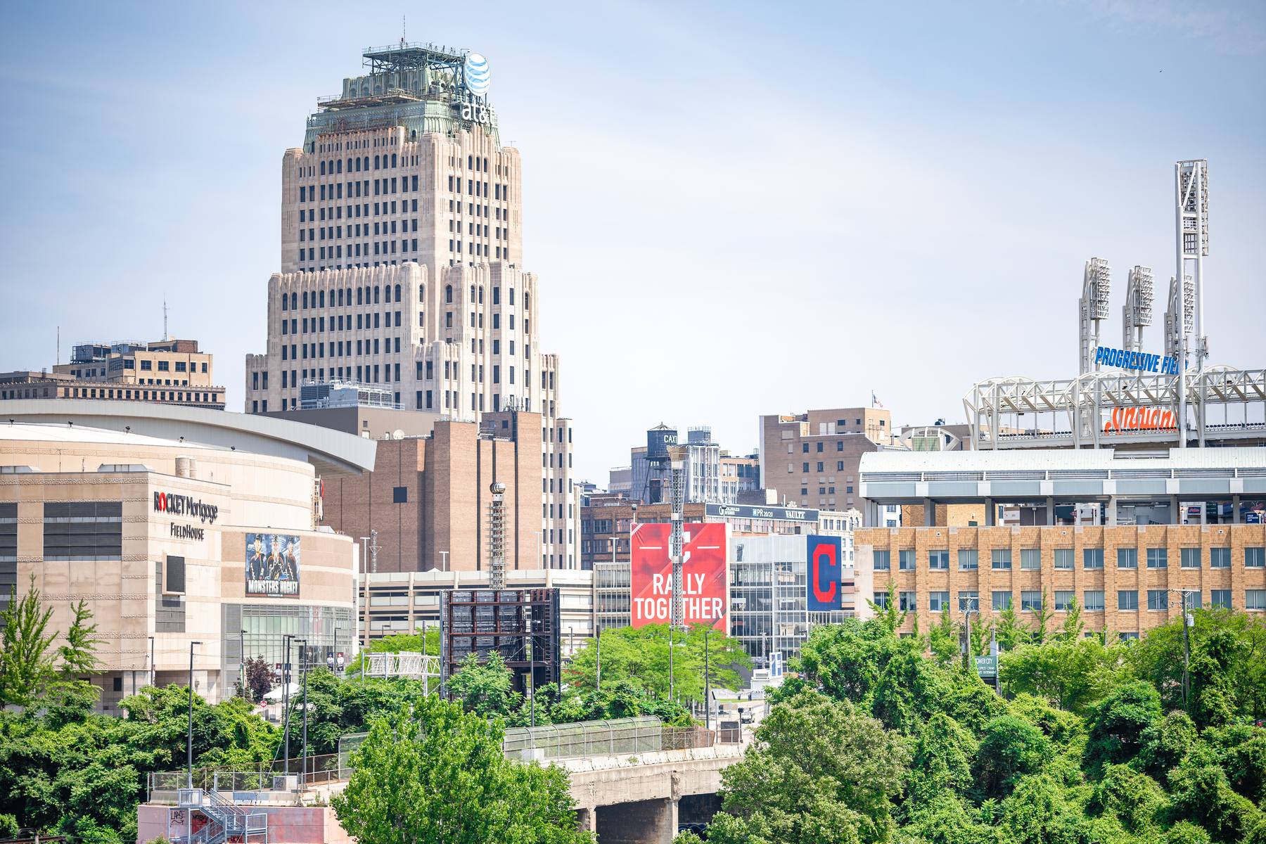 Progressive Field seen across downtown Cleveland, a historic office tower in the foreground and the ballpark's light towers beyond