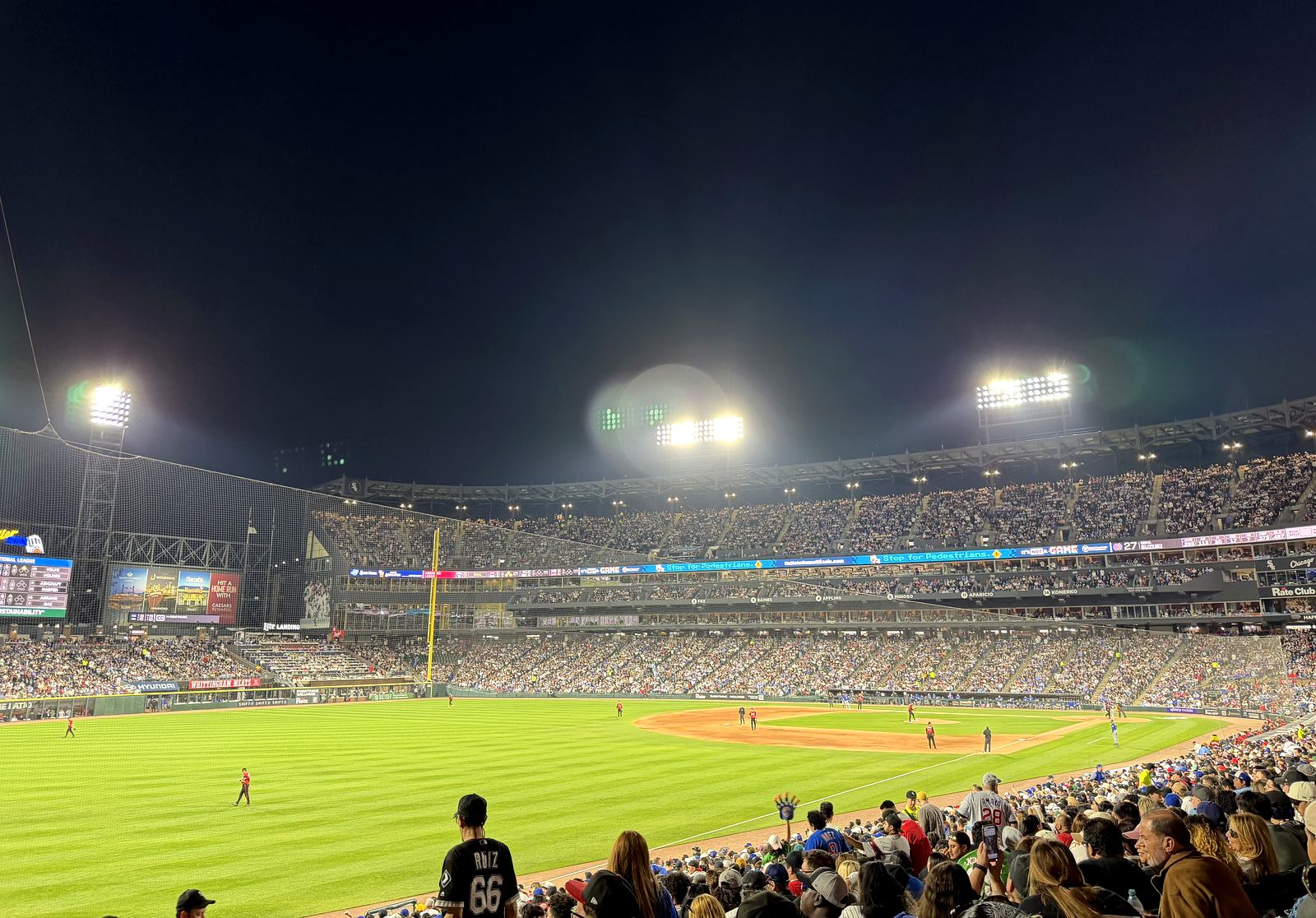 Rate Field at night with the bowl and centerfield scoreboard lit up and a full crowd in the stands