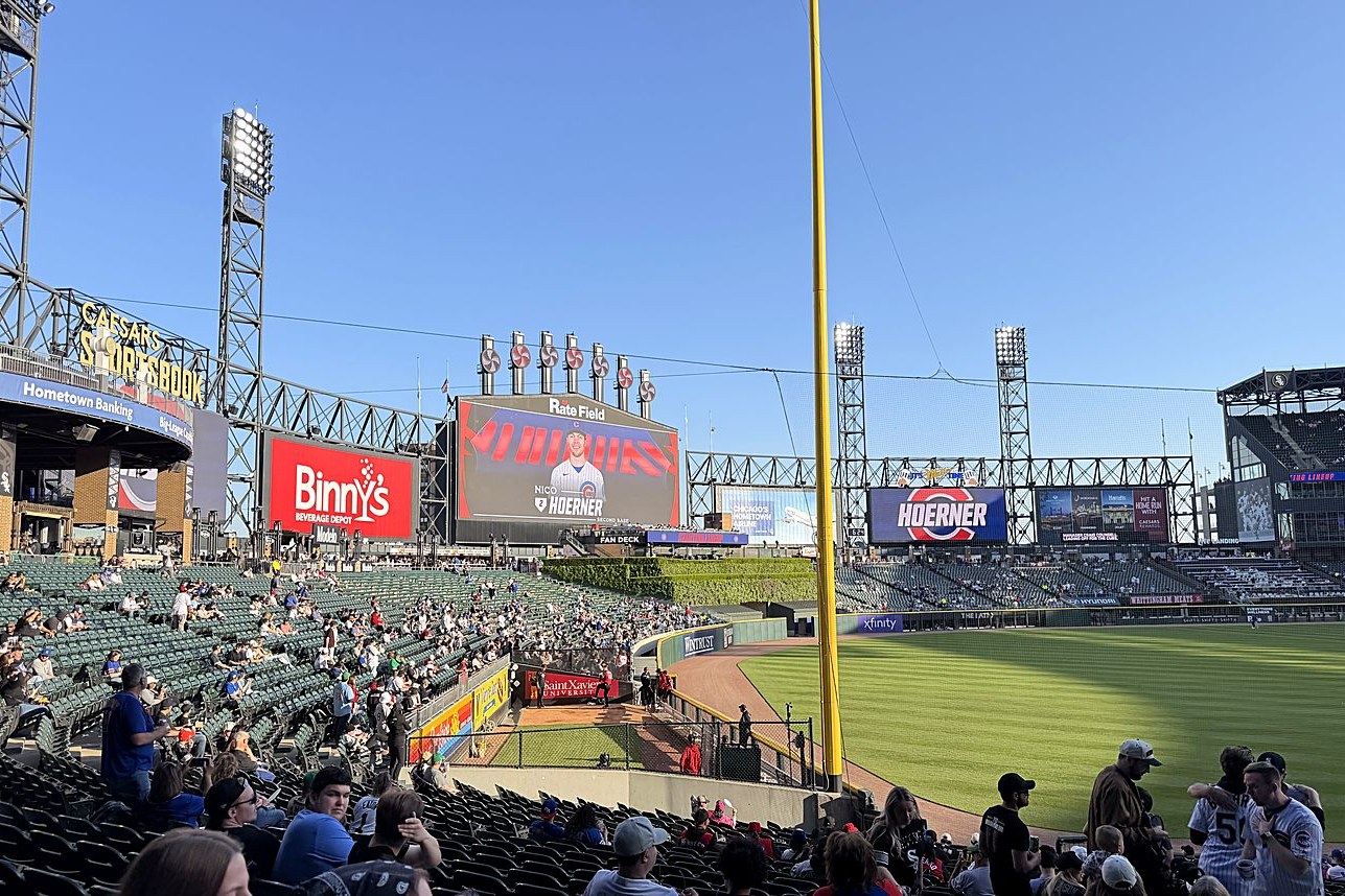 Rate Field in golden evening light, the outfield and center-field scoreboard seen from a lower-bowl seat near the foul pole