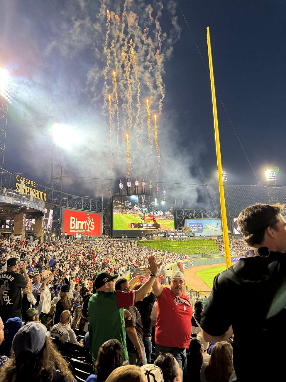 A summer night game at Rate Field with the centerfield scoreboard lit up