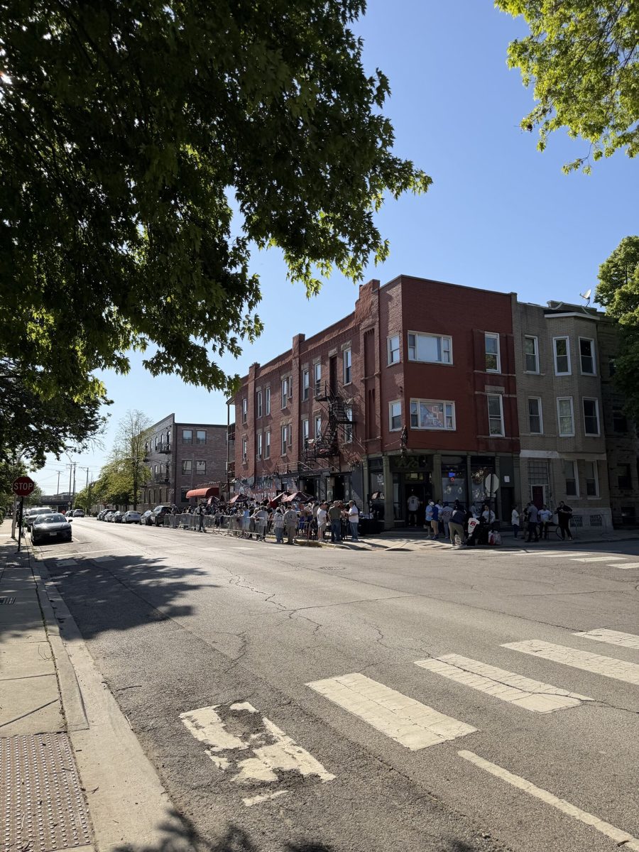 A Bridgeport residential streetscape near Rate Field on a Sox game day, with brick walk-up apartments lining the street and afternoon sun overhead