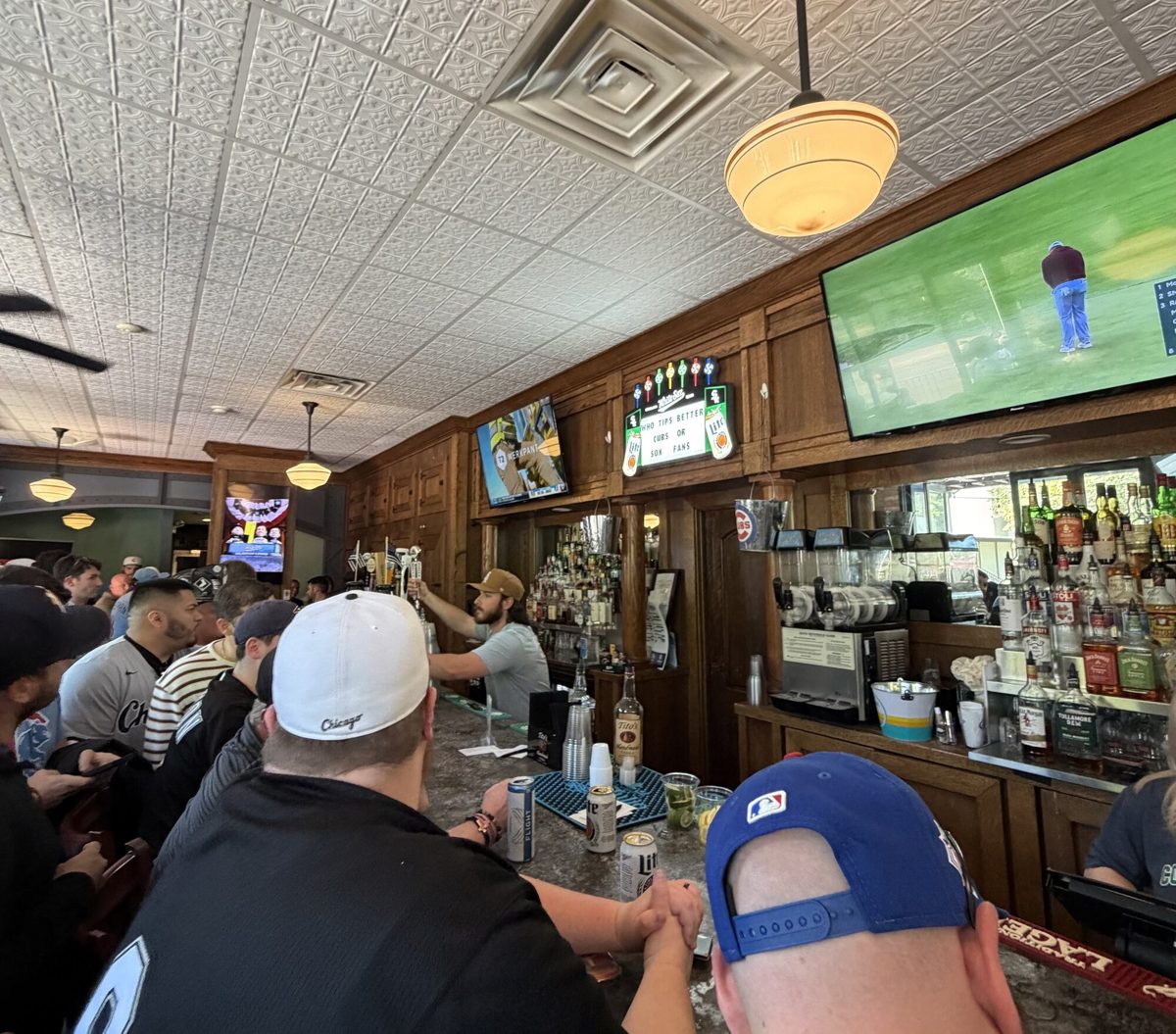 The packed interior of Cork & Kerry at the Park on a Sox game day, with fans at the rail under overhead pendant lighting and game broadcasts on the TVs
