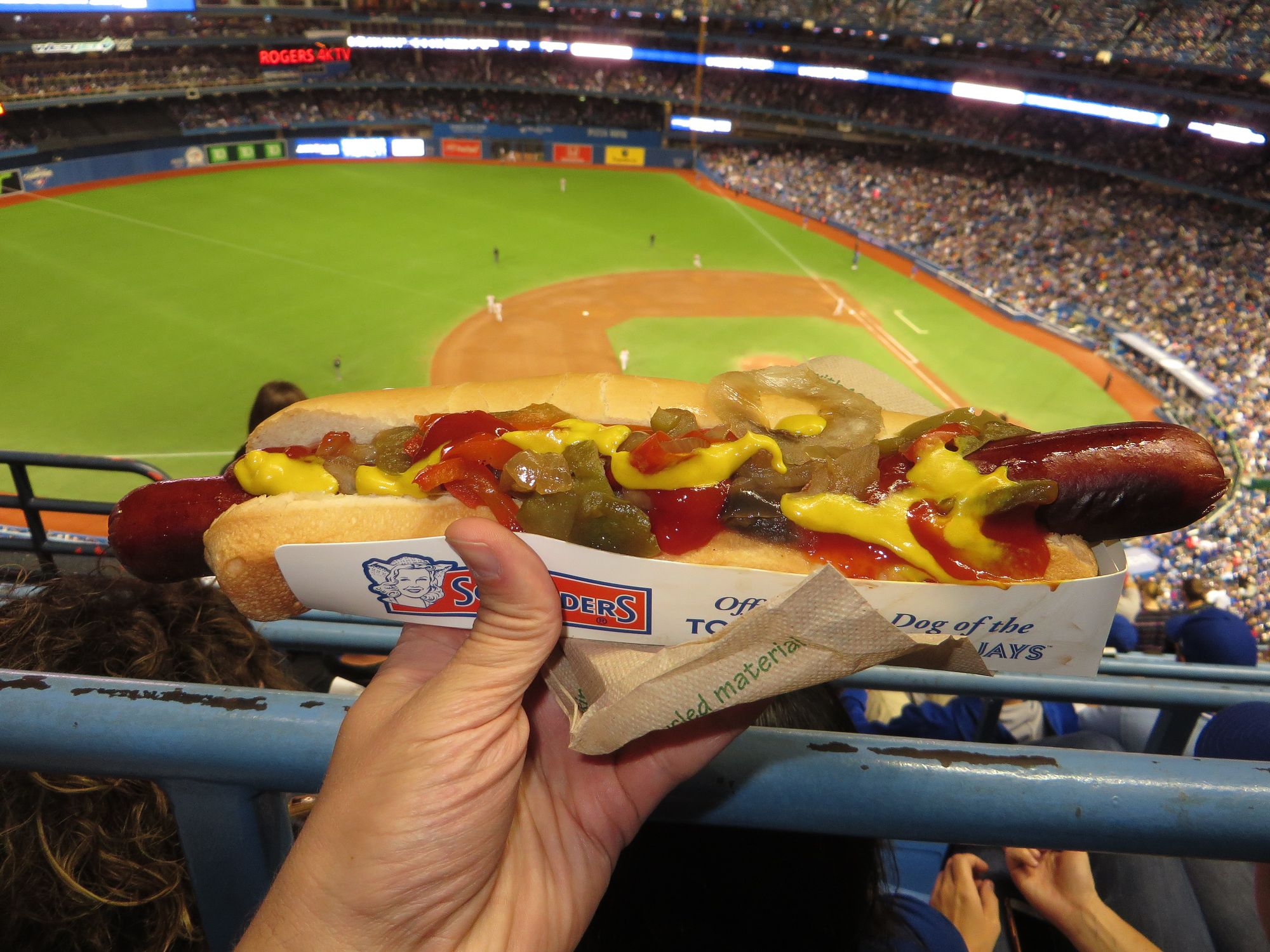 A loaded footlong hot dog held up over the Rogers Centre bowl during a Blue Jays game