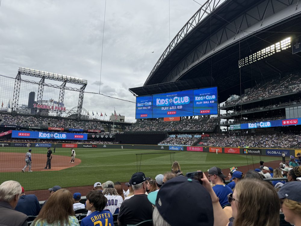The view from field-level seats at T-Mobile Park on an overcast day, the retractable roof panels parked on their rails beyond right field and Kids Club boards on the outfield wall