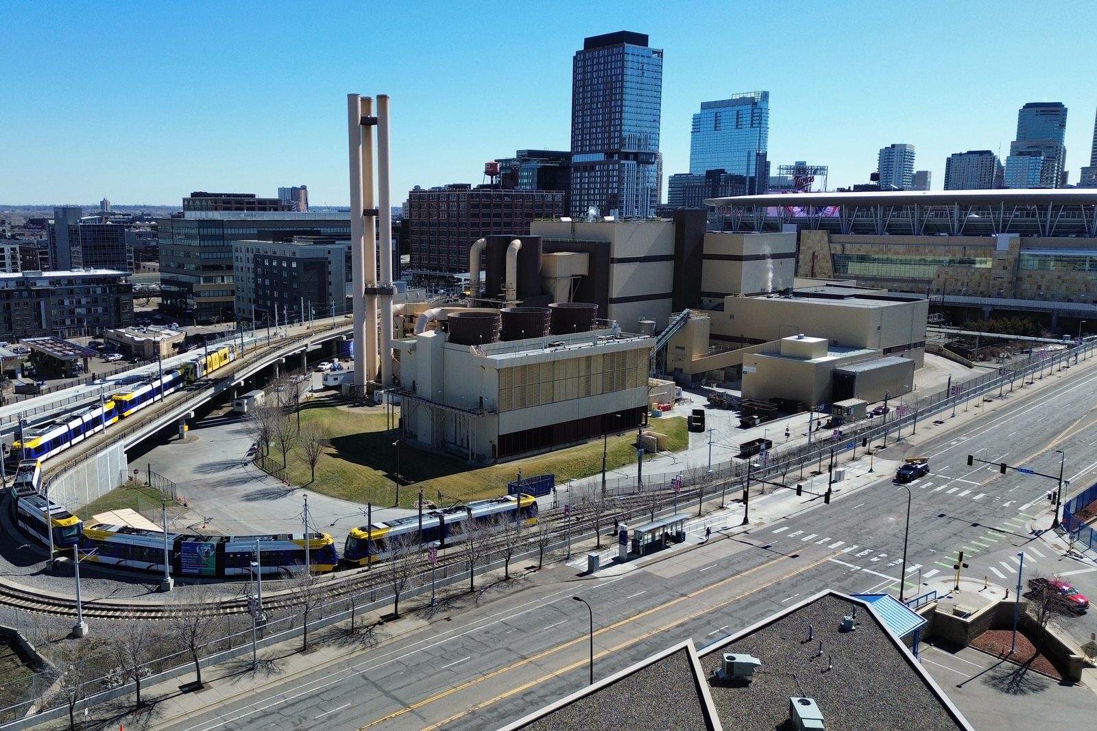 METRO light rail trains at Target Field Station, the ballpark's white canopy roof and Twins signage visible in the background skyline