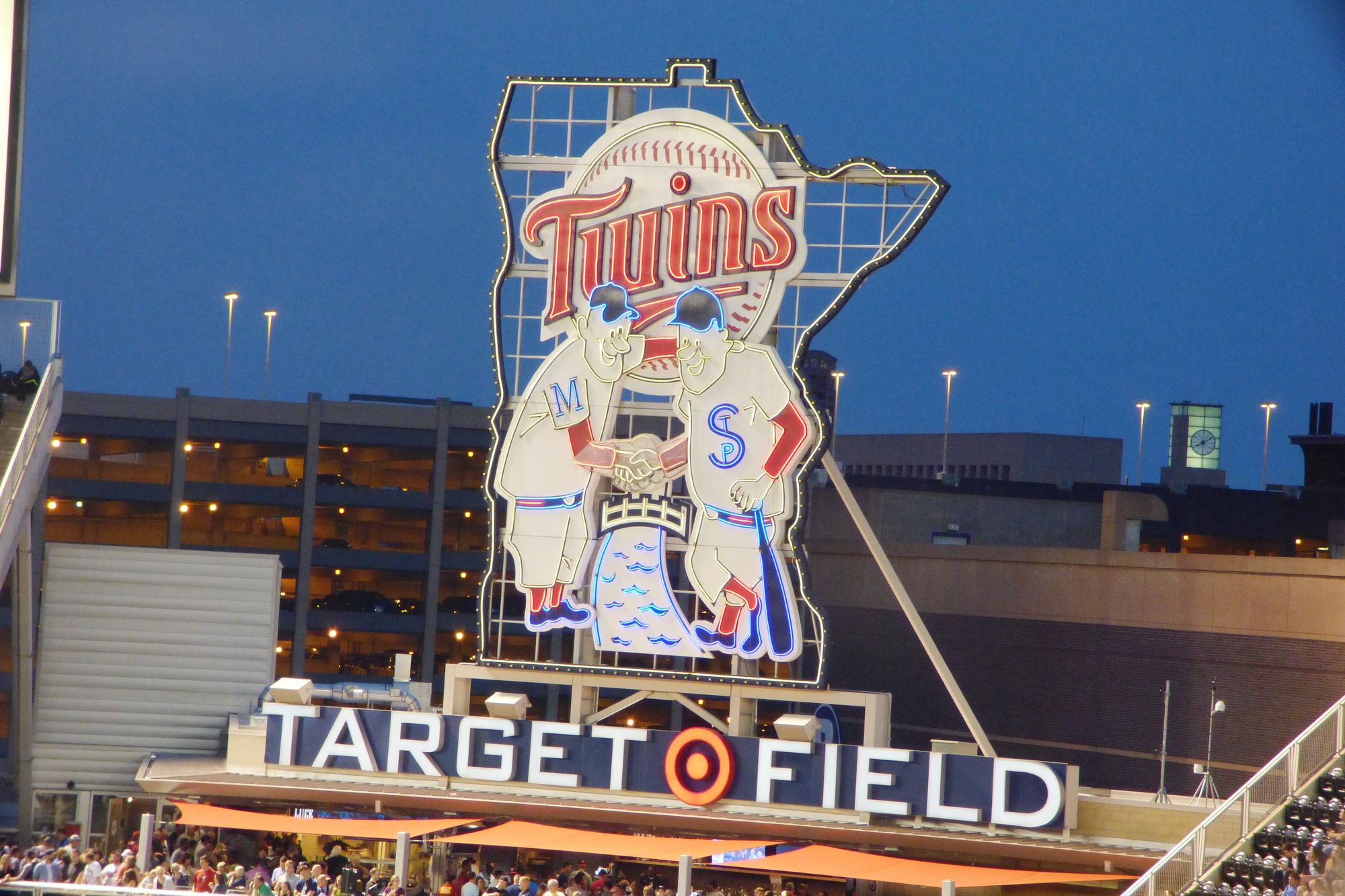 The Minnie and Paul celebration sign above Target Field, the two players shaking hands across the Mississippi River, lit against a dusk sky