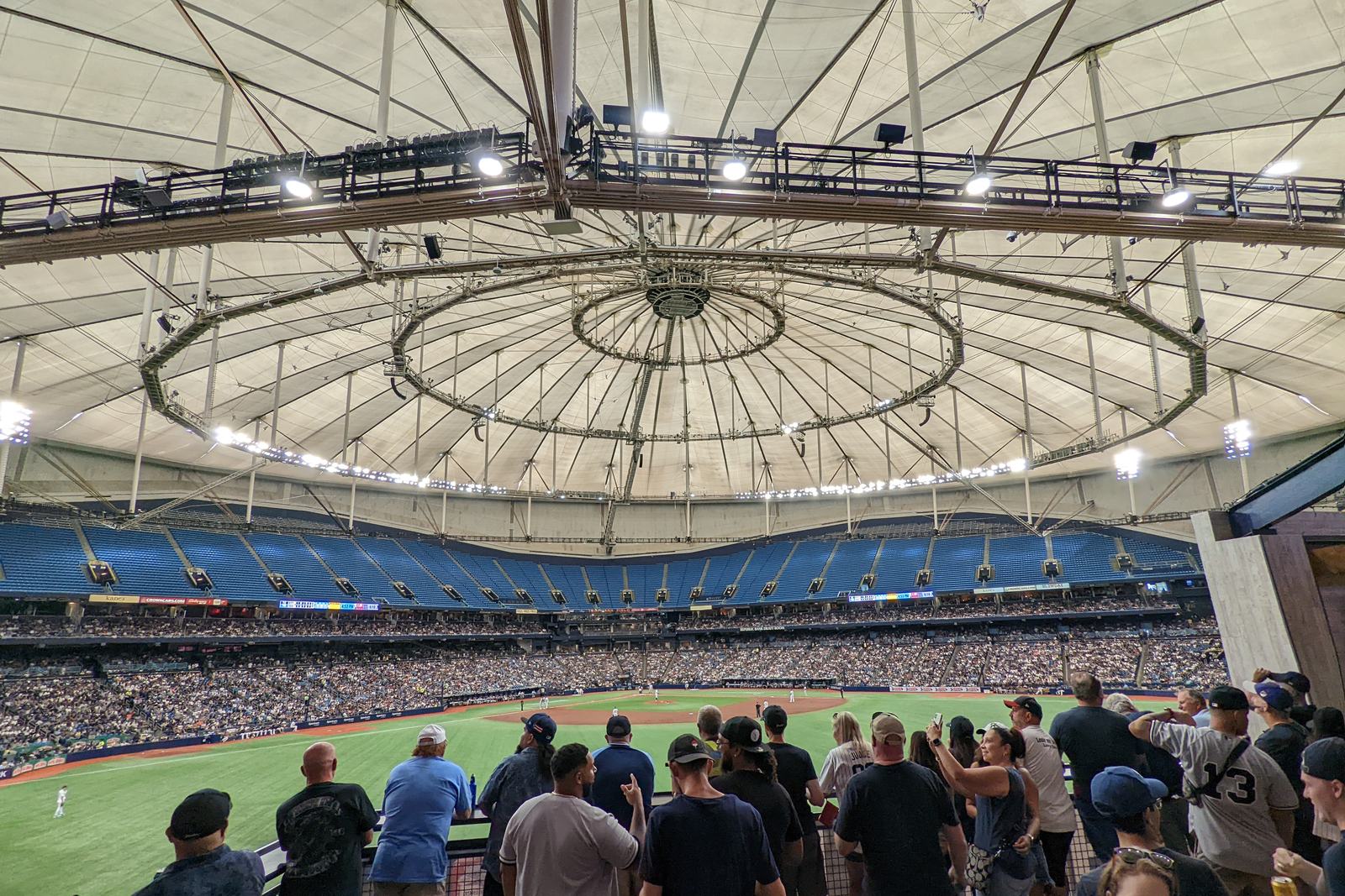 Fans in the stands at Tropicana Field looking out over the field, the catwalk rings of the dome overhead